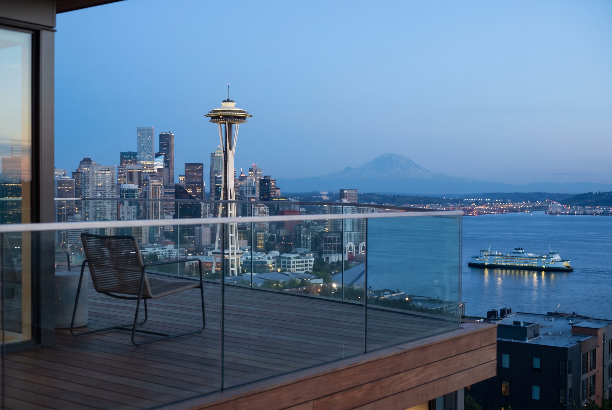 Dusk view from a Seattle condominium terrace: the Space Needle and downtown skyline, a ferry on Elliott Bay, and Mount Rainier on the horizon